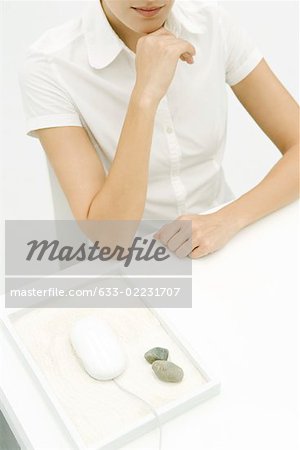 Woman sitting at desk, computer mouse nearby in rock garden, high angle view, cropped