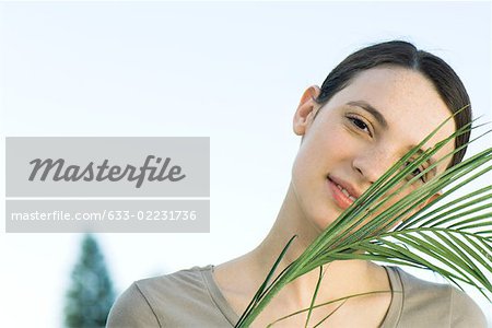 Jeune femme avec des feuilles de palmier, souriant à la caméra