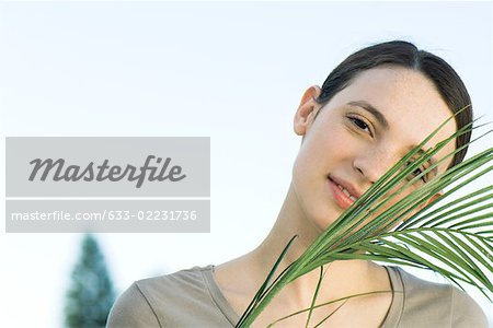 Young woman with palm leaf, smiling at camera