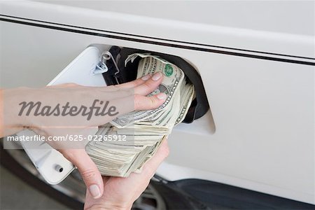 Close-up of a person's hands putting US paper currency in a gas tank of a car