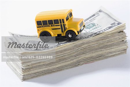 Close-up of a toy school bus on a stack of US dollar bills