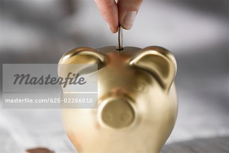 Close-up of a person's hand putting a coin into a piggy bank
