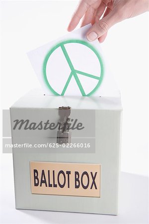 Close-up of a person's hand inserting a world peace symbol vote into a ballot box