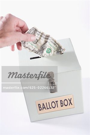 Close-up of a person's hand inserting a US dollar bill into a ballot box