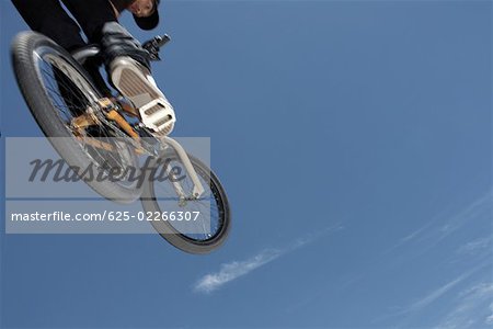 Vue d'angle faible d'un jeune homme sautant avec sa bicyclette