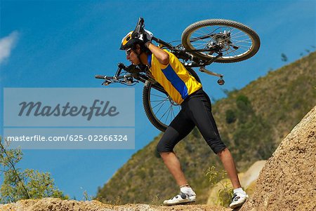 Side profile of a young man carrying a mountain bike on his shoulders