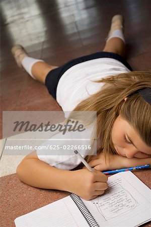 Schoolgirl lying on the floor and writing in a spiral notebook