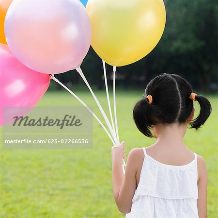 Rear view of a girl holding balloons in a park