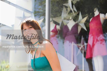 Side profile of a young woman carrying a shopping bag in front of a clothing store