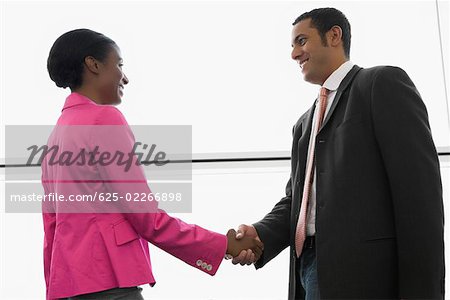 Side profile of a businessman and a businesswoman shaking hands at an airport