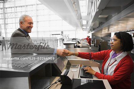 Side profile of a businessman shaking hands with an airline check-in attendant and smiling