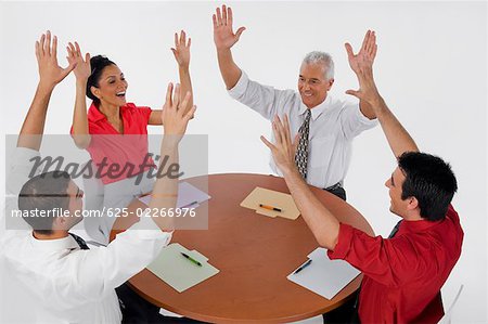Trois hommes et une femme d'affaires souriant avec leurs bras levés lors d'une réunion