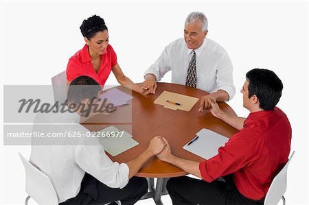 Three businessmen and a businesswoman praying with holding their hands in a meeting