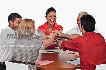 Three businessmen and two businesswomen stacking hands on top of each other in a meeting