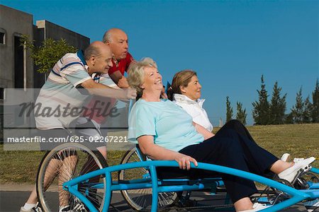 Two senior women sitting on a quadracycle and two senior men pushing it