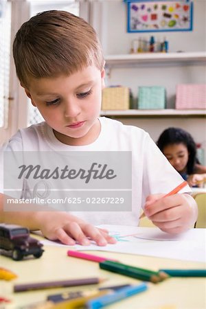 Gros plan d'un garçon de dessin sur une feuille de papier avec une fille assise derrière lui