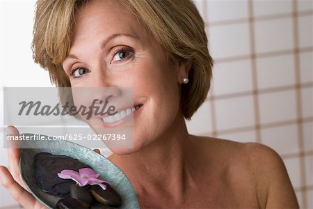 Porträt einer reifen Frau hält eine Schüssel mit Kieselsteinen und eine Blume
