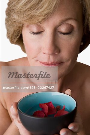 Close-up of a mature woman holding a bowl of water with floating flowers