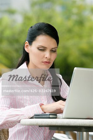 Close-up of a businesswoman using a laptop at a sidewalk cafe