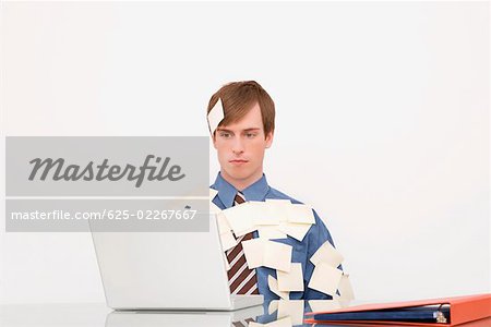 Businessman covered with adhesive notes and working on a laptop