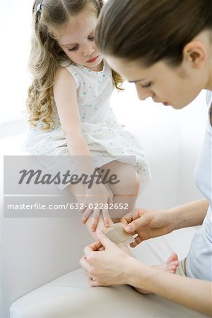 Mother putting adhesive bandage on young daughter's leg