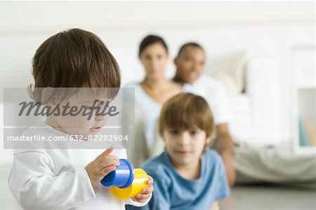 Kleinkind Mädchen spielt mit Spielzeug, Familie, die gerade im Hintergrund