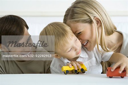 Petit garçon assis avec leurs parents, jouer avec des camions-jouets, mère fouinais sa joue