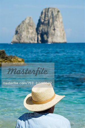 Man Sitting on the Beach, the Faraglioni in the Distance, Gulf of Naples, Capri, Naples, Campania, Italy