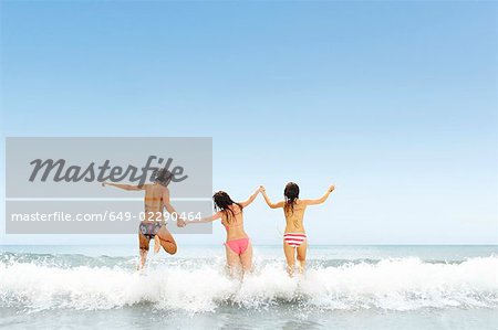 Three girls jumping over wave