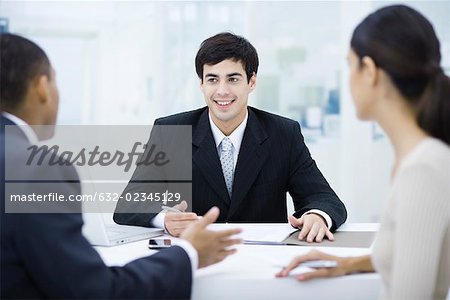 Businessman sitting at desk, talking with clients and smiling