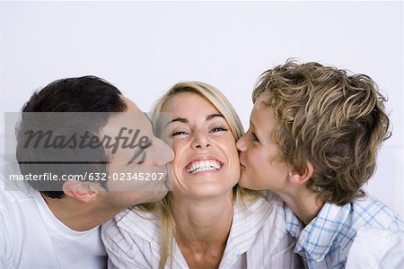 Femme souriante étant embrassée sur chaque joue son mari et le jeune fils