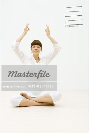 Woman sitting in lotus position on floor, arms raised