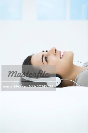 Young woman listening to headphones, looking up, smiling