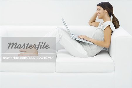 Teenage girl reclining on couch, using laZSop, side view