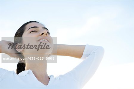 Woman with eyes closed, hands behind head