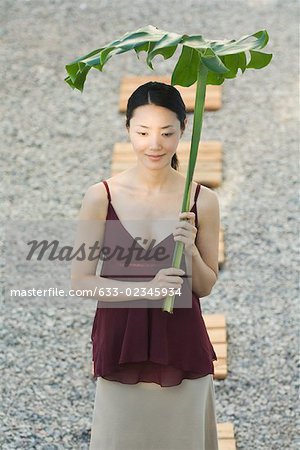 Woman walking in rock garden, holding palm frond over head