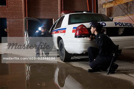 Police Officers Crouching Behind Police Car With Guns Drawn