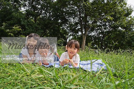 Drei Mädchen auf Gras in einer Zeile liegend