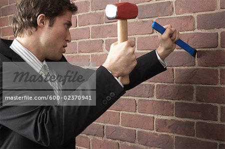 Businessman using Mallet and Chisel on Brick Wall