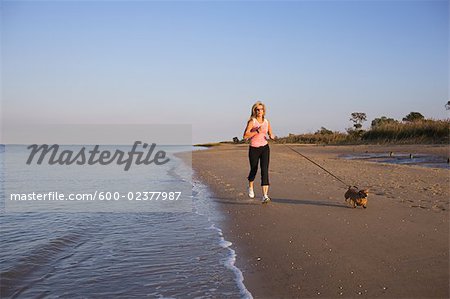 Femme en cours d'exécution sur la plage avec chien