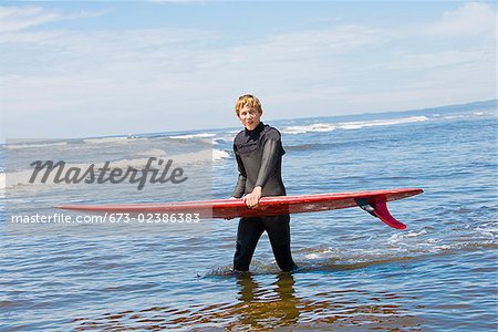 Surfer carrying a surfboard in water, Washington State, USA