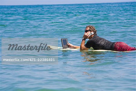 Man talking on a phone and using a laptop in the sea