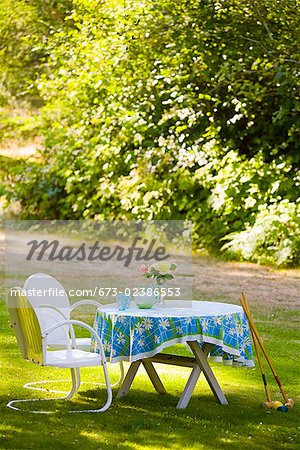 Two chairs with a table and croquet mallets in a garden