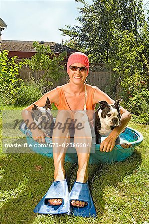 Femme assise dans une piscine pour enfants avec deux Terriers de Boston