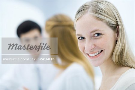 Young professional woman smiling at camera, colleagues talking in background