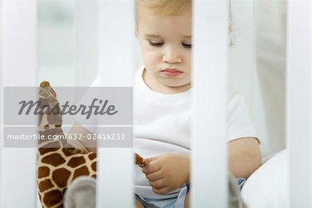 Toddler sitting in crib, playing with stuffed giraffe