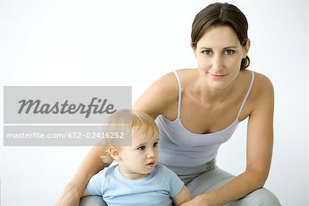 Woman smiling at camera, toddler standing between legs