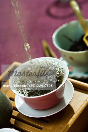 Eau chaude étant coulé et éclabousser sur les feuilles de thé dans une tasse de thé