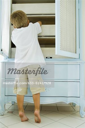 Boy reaching inside armoire, rear view