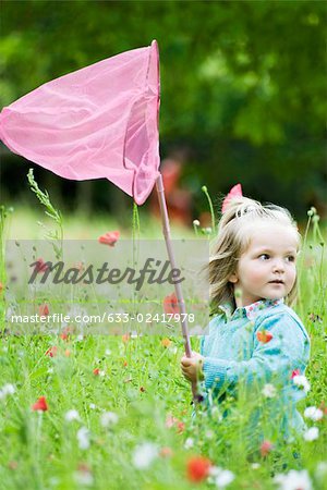 Girl holding up butterfly net, standing in field of flowers